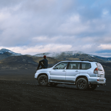 person sitting on hood of SUV by mountains