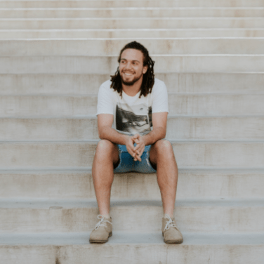 man with long hair smiling sitting on steps