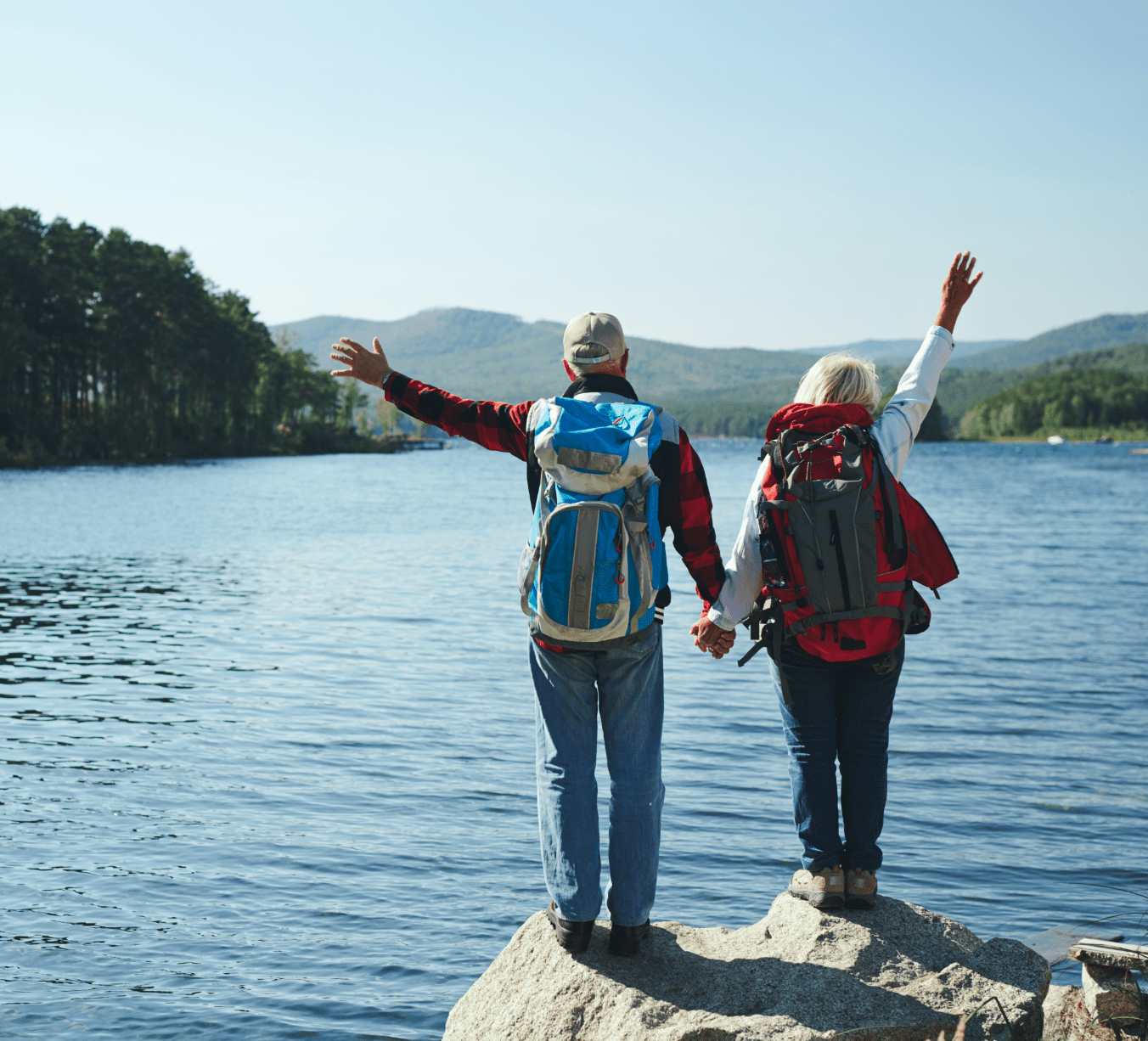 senior couple wearing backpacks facing lake