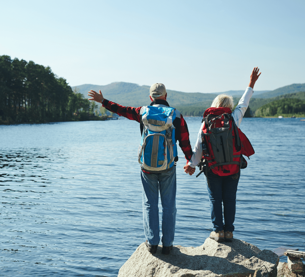 senior couple wearing backpacks facing lake